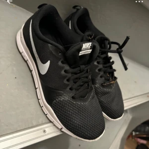Svarta Nike sneakers - Säljer ett par svarta Nike sneakers i bra skick. De har en vit sula och den klassiska Nike-loggan i vitt på sidan. Skorna har snörning och är perfekta för vardagsbruk eller träning. Lite slitage på sulan men annars i fint skick.