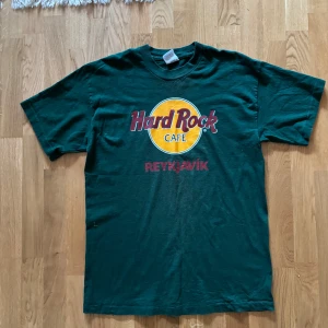 Grön Hard Rock Café T-shirt från Reykjavik - Säljer en grön T-shirt från Hard Rock Café med tryck från Reykjavik. Den har ett stort, färgglatt tryck på framsidan med texten 'Hard Rock Café Reykjavik' i rött och gult. På baksidan står det 'SAVE THE PLANET' i rött. 
