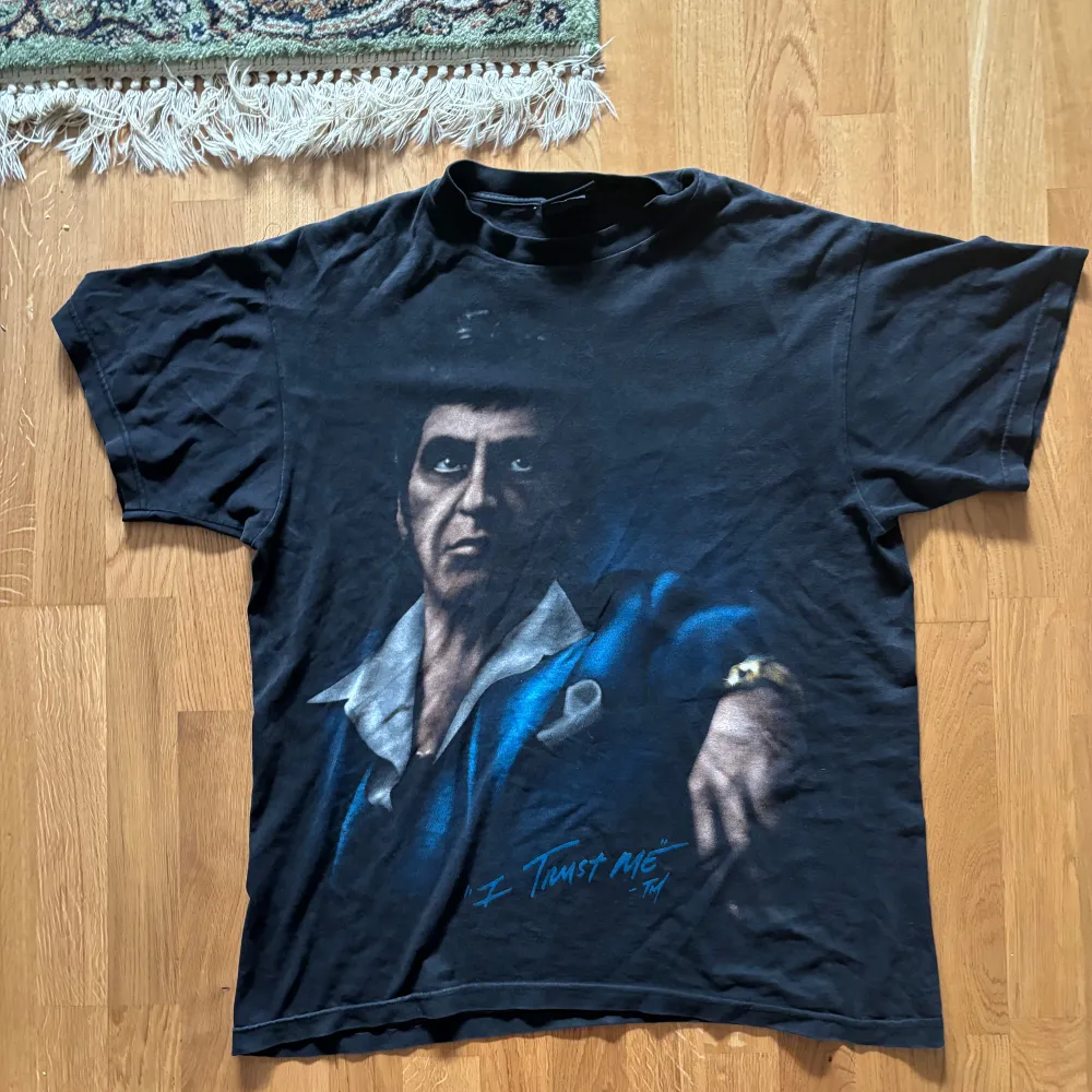 Säljer en svart t-shirt med ett stort tryck av en ikonisk karaktär från Scarface. T-shirten har en cool vintage-look med korta ärmar och en avslappnad passform. Perfekt för filmälskare eller som statement-plagg i garderoben.. T-shirts.