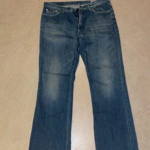 Blå jeansbyxor - Säljer ett par klassiska blå jeansbyxor med en avslappnad passform. De har en lätt slitning på framsidan och en rak benform. Perfekta för en casual look! Bootcut och baggy