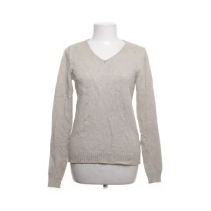 Beige stickad tröja - Säljer en stilren beige stickad tröja med v-ringning. Tröjan har långa ärmar och ribbade muddar vid ärmslut och nederkant. Perfekt för kyligare dagar.