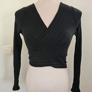 Snygg svart omlottopp från Shein i ribbat material. Toppen har en v-ringad design och långa ärmar, perfekt för en stilren look. Passar bra till både jeans och kjol.