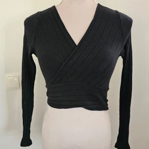 Svart omlottopp från Shein - Snygg svart omlottopp från Shein i ribbat material. Toppen har en v-ringad design och långa ärmar, perfekt för en stilren look. Passar bra till både jeans och kjol.