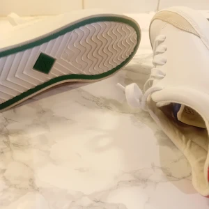 Vita sneakers från Gant - Snygga vita sneakers från Gant med snörning och detaljer i beige och rött. Skorna har en grön sula och är perfekta för en stilren look. Helt nya och oanvända 
