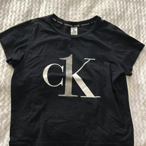 Svart t-shirt från Calvin Klein - Snygg svart t-shirt från Calvin Klein med stort 'ck' tryck på framsidan. Den har en rund halsringning och korta ärmar. Perfekt för en casual look.