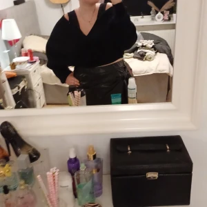 Svart kjol med knytband - Snygg svart kjol i skinnimitation med ett dekorativt knytband i midjan. Perfekt för att ge en edgy touch till din outfit. Kjolen har en kort längd och en glansig finish.