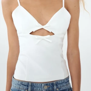 Vit linnetopp med rosett - Snygg vit linnetopp med smala axelband och två söta rosetter framtill. Toppen har en liten utskärning under bysten som ger en trendig look. Perfekt för varma sommardagar. jätte fint skick 🫰🏻🫰🏻