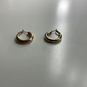 Guldiga hoop-örhängen - Säljer ett par stilrena guldiga hoop-örhängen. Perfekta för att ge en elegant touch till din outfit. De är enkla att matcha med andra smycken och passar till många tillfällen.