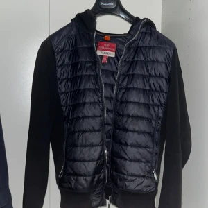 Svart fleecejacka från Parajumpers - Snygg svart fleecejacka från Parajumpers med quiltad framsida och dragkedja. Jackan har en broderad logga på ärmen och är perfekt för kyligare dagar. Den kombinerar stil och funktionalitet med sina praktiska fickor. Skick 810 inga skador på jackan  ( barnstorlek) 