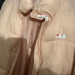 Ljusrosa Jacka från FILA - Säljer en snygg ljusrosa jacka från FILA med dragkedja och hög krage. Perfekt för kyligare dagar. Jackan har en stilren design med FILA-logga på bröstet. Denna jackan är min lillasysters (hon vill sälja den då hon ska flytta) så det finns inga bilder när jag har denna jackan på mig tyvärr. Jackan är även väl använd men är ändå i bra skick.