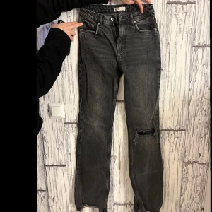 Grå bootcut jeans med slitningar - Snygga grå bootcut jeans med slitningar på knäna. De har en klassisk femficksdesign och knappgylf. Perfekta för en avslappnad stil.