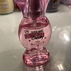 Candy Pink Eau de Parfum från Flor de Mayo   - Söt och lekfull parfym i en rosa flaska formad som en klänning. Candy Pink från Flor de Mayo ger en fräsch och ungdomlig doftupplevelse. Perfekt för dig som älskar söta och fruktiga dofter. Flaskan är både dekorativ och praktisk att ha med sig.