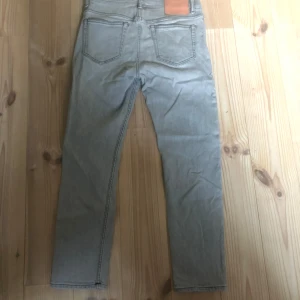 Grå jeansbyxor från Acne Studios - Snygga grå jeansbyxor från Acne Studios med en klassisk femficksdesign. Byxorna har en knappgylf och en läderpatch med logotyp baktill. Perfekta för en stilren look. Nypris 4000