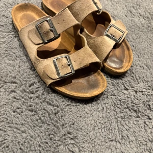 Bruna sandaler - Säljer ett par klassiska bruna sandaler med dubbla justerbara spännen. Sandalerna har en bekväm fotbädd och är perfekta för sommarens äventyr.