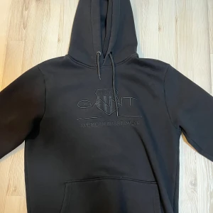 Svart hoodie från GANT - Säljer en stilren svart hoodie från GANT. Tillverkad i 100% bomull för en mjuk och bekväm känsla. Perfekt för en avslappnad look. Jätte bra kvalité på den, har inte haft den så länge. Storlek M. Pris går att diskutera.