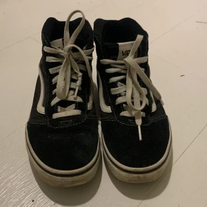 Svarta sneakers från Vans - Säljer ett par klassiska svarta Vans sneakers med vit sula och snörning. Skorna har den ikoniska vita sidostripen och är perfekta för en avslappnad stil.