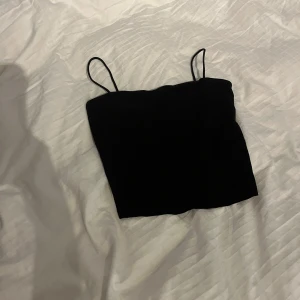 Svart linne från Gina Tricot - Snygg svart tubtopp från Gina Tricot med smala axelband. Perfekt för en stilren look. Enkel och mångsidig topp som passar till många olika outfits.