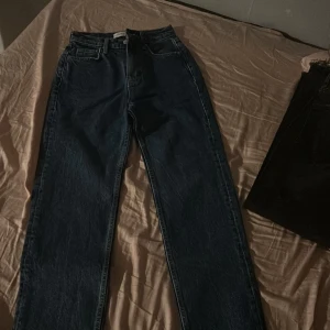 Mörkblå jeans med fransade kanter - Snygga mörkblå jeans med hög midja och fransade kanter. De har en klassisk femficksdesign och stängs med dragkedja och knapp. Perfekta för en avslappnad stil.