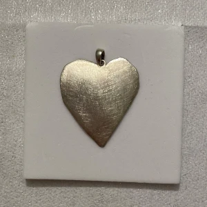 Hjärta i silver - Elegant hängsmycke i form av ett hjärta, tillverkat i silver. Perfekt för att ge en personlig touch till ditt halsband. Den borstade ytan ger en stilren och modern känsla. Längd 4,5cm, bredd 3,5cm. 925 stämplad.