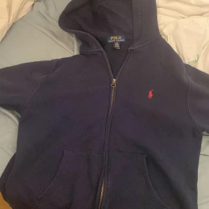 hoodie från Polo Ralph Lauren - Säljer en snygg mörkblå hoodie från Polo Ralph Lauren med dragkedja och huva. Perfekt för en avslappnad stil. Inga defekter på tröjan över huvud taget! Hör av dig vid Minsta lilla bekymmer!