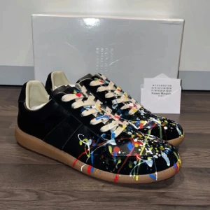 Masion Margiela GATS - Unika svarta sneakers från Maison Margiela med färgstänk i blått, rött, gult och vitt. Skorna har en klassisk design med snörning och en brun sula. Perfekta för dig som vill sticka ut med en konstnärlig touch.