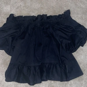 Svart offshoulder blus - Snygg svart offshoulder blus med volangdetaljer. Perfekt för en stilren look. Passar bra till både jeans och kjol.