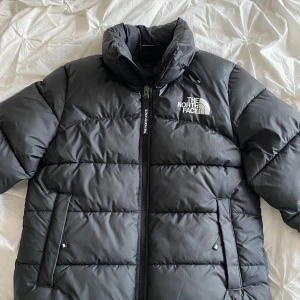 The North Face jacka - Säljer en svart dunjacka från The North Face med dragkedja och hög krage. Jackan har en pufferdesign och två praktiska fickor framtill. Perfekt för kyliga dagar. Den har även en luva som man kan ta ut från nacken🥰