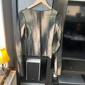 Mönstrad långärmad topp från Weekday - Säljer en unik långärmad topp från Weekday i storlek XS. Toppen har ett abstrakt mönster i dova färger som grön, brun och svart. En skada vid nacken som man kan se på bild 3.