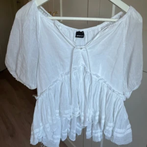 Vit blus/topp - Säljer en söt vit blus från Gina Tricot med korta ärmar, volangdetaljer och en knytning framtill. Toppen är i nyskick då jag bara använt den två gånger. För fler frågor och funderingar, skriv!
