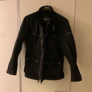 Barbour jacka  - Säljer en stilren svart jacka från Barbour i storlek M. Jackan har en quiltad insida med röd detalj och flera praktiska fickor. Den är i väldigt gott skick (9/10) och perfekt för vår och höst. Nypris 4200kr