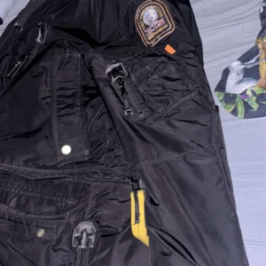 Svart jacka från Parajumpers - Säljer en svart jacka från Parajumpers Masterpiece Series. Jackan har flera fickor med dragkedja och knappar, samt en broderad logga på ärmen. Perfekt för kyligare väder.