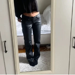 Svarta skinnbyxor - Snygga svarta skinnbyxor med låg midja och bootcut-stil. Byxorna har en tight passform och är perfekta för en trendig look. De har fickor både fram och bak samt en dragkedja framtill.