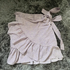 Lila blommig omlottkjol från Shein - Säljer en superfin lila omlottkjol från Shein med ett sött blommönster. Kjolen har volanger och ett knytband i midjan för en perfekt passform. Perfekt för vår och sommar! 🌸