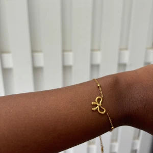 Guld rosett armband  - Ett stilfullt guldfärgat armband i rostfritt stål med delikata pärlor och en elegant rosettdesign.