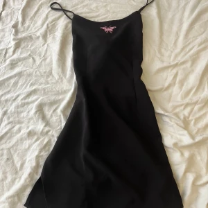 Svart kort klänning  - En svart kort klänning med öppen rygg och en rosa fjäril på framsidan.