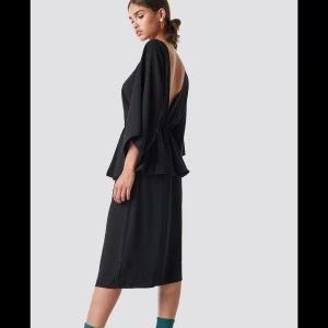 Svart klänning med öppen rygg - Säljer en elegant svart klänning med öppen rygg och volangdetaljer. Klänningen har trekvartsärmar och en bekväm passform som passar perfekt för festliga tillfällen. Materialet är mjukt och följsamt, vilket gör den både stilren och bekväm.