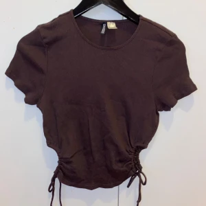 Brun ribbad topp från H&M Divided - Säljer en brun ribbad t-shirt från H&M. Den har en snygg knytdetalj i midjan som ger en fin passform. Perfekt för vardags eller skola nu i höst 🍂👌🏽Den är i storlek L men skulle snarare säga mer som en M