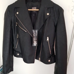 River Island Bikerjacka Ny/Oanvänd!!! - Superfin River Island bikerjacka/skinnjacka i fejk-läder i storlek S. Aldrig använd och pris-märkes-lappen finns kvar. Dragkedja fram och vid ärmsluten. 