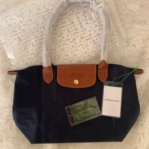 Longchamp Le Pliage Väska - strl M - Longchamp Le pilage liknande väska i storlek M - i marinblå. Helt oanvänd. Plast kvar på handtagen och på dragkedjan. Alla delar medföljer som syns på bilden. Mått syns på sista bilden. Skriv vid frågor eller funderingar ☺️☺️Obs! Detta är en ”liknande”