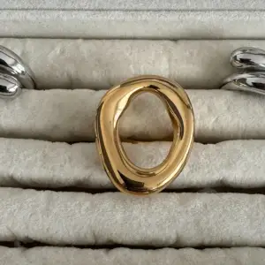 Säljer en unik guldfärgad ring med en cool, organisk form. Den har en öppen design som ger den ett modernt och stilrent utseende. Perfekt för att ge din outfit en extra touch av elegans!