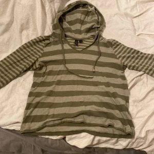 Randig hoodie i grönt och beige - Säljer en supermysig randig hoodie i grönt och grått. Den har en avslappnad passform och är perfekt för både höst och vår. Tröjan har en huva med snören och långa ärmar. Perfekt för chill dagar eller när du bara vill vara bekväm. (Tunnt material) 🧡