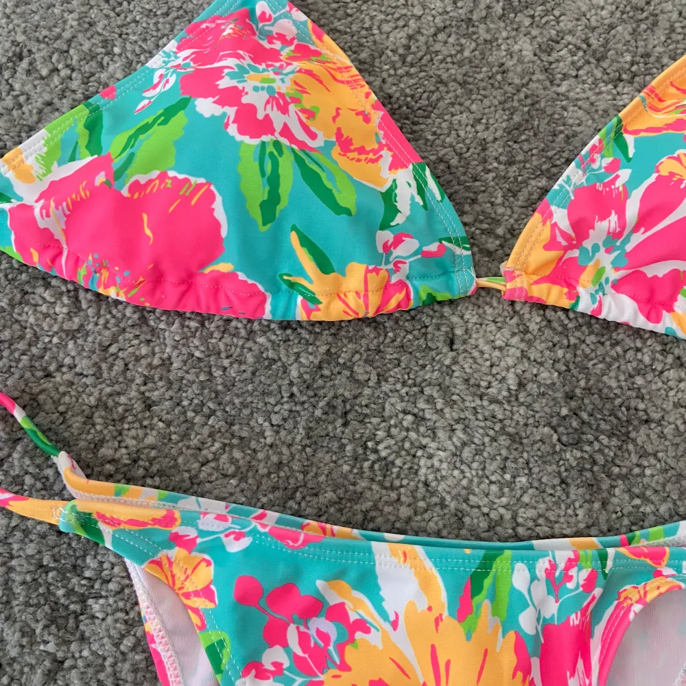 Säljer en superfin och färgglad bikini med blommigt mönster i rosa, gul och grön. Den har en klassisk trekantsmodell med knytband i nacken och ryggen. Perfekt för sommarens stranddagar!. Övrigt.