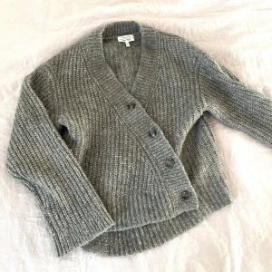 Grå stickad kofta från & Other Stories - Säljer en supermysig grå stickad kofta från & Other Stories. Den har en snygg v-ringning och knappar framtill. Perfekt för höst och vinter när du vill hålla dig varm och stilren. Koftan är i storlek XS! 🧶