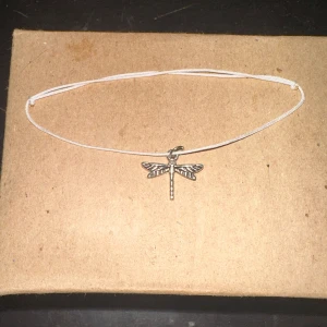 Silverfärgat armband med trollslända - Ett enkelt och stilrent armband med en silverfärgad trollslända som hänge. Perfekt för att lägga till en subtil touch av naturinspirerad elegans till din outfit. Armbandet har en tunn rem som gör det lätt och bekvämt att bära.