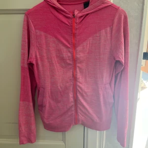 Rosa hoodie med dragkedja - Säljer en snygg rosa hoodie med dragkedja framtill. Den har en skön luva och långa ärmar, perfekt för kyliga dagar. Materialet känns mjukt och bekvämt, och den har en cool, avslappnad stil. Passar perfekt till träning!