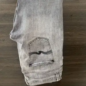 Säljer ett par grå jeans från Nudie Jeans i storlek 33/34. De har en klassisk femficksdesign med en snygg broderad detalj på bakfickan. Jeansen är i bra skick och har en dragkedja framtill😁