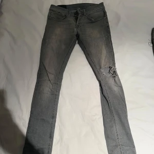 Grå jeans från Dondup - Säljer ett par grå jeans Dondup i ok skick. De har en cool sliten look med en reva på ena benet. Perfekta för en avslappnad stil! De har en klassisk femficksdesign och knappar i midjan. Passar perfekt till både vardag och fest.