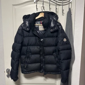  Moncler Chevalier - Säljer en snygg svart dunjacka från Moncler i  okej skick. Jackan har en quiltad design med dragkedja och knappar, samt en luva för extra värme. Perfekt för kalla vinterdagar! Jackan är äkta och köpt från KaspersHeat för drygt 2 år sedan.