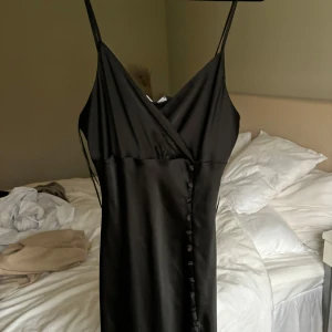 Svart  klänning - Säljer en elegant svart klänning. Den har en omlott-design med knappar framtill! Perfekt för festliga tillfällen eller en utekväll. Klänningen är i nytt skick och har en smickrande passform. Lappen kvar, nypris 359 kr❣️