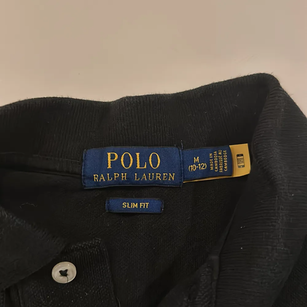 Säljer en snygg svart pikétröja från Ralph Lauren i slim fit. Den har en klassisk krage och korta ärmar, med det ikoniska röda logotypbroderiet på bröstet. Perfekt för både vardag och fest! 🖤. Tröjor & Koftor.